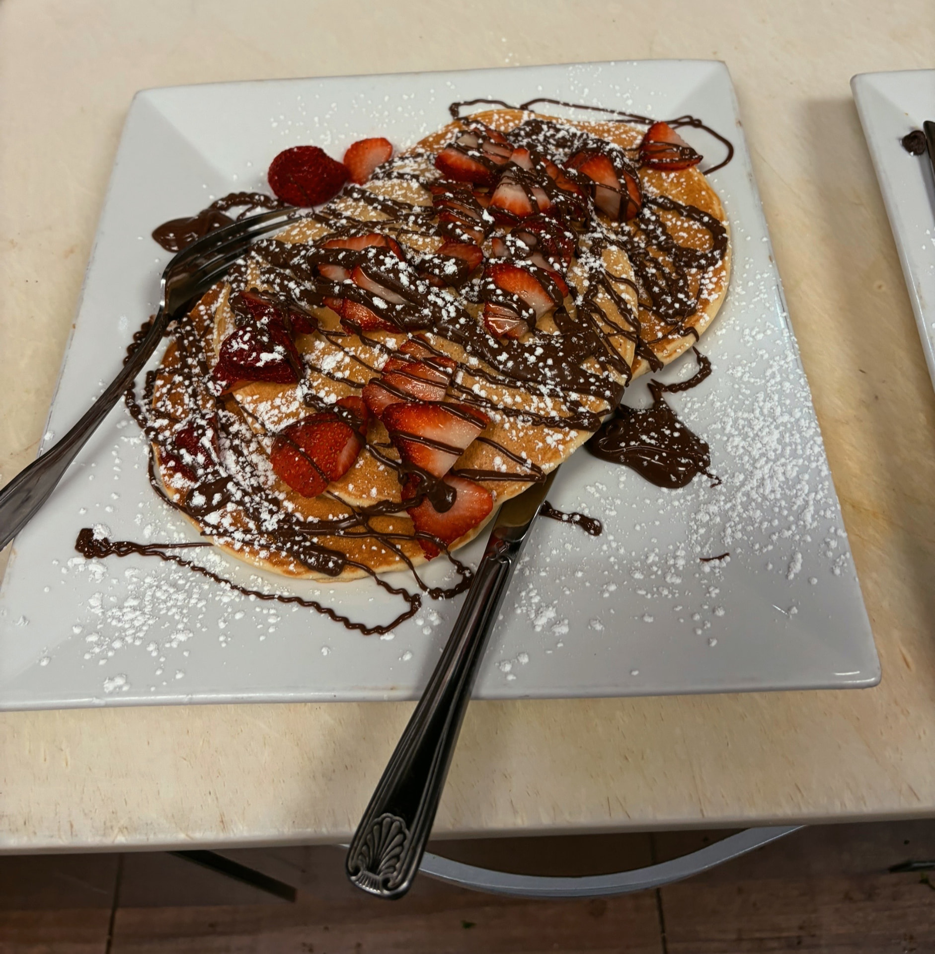 Pancakes topped with strawberries, chocolate drizzle and powdered sugar